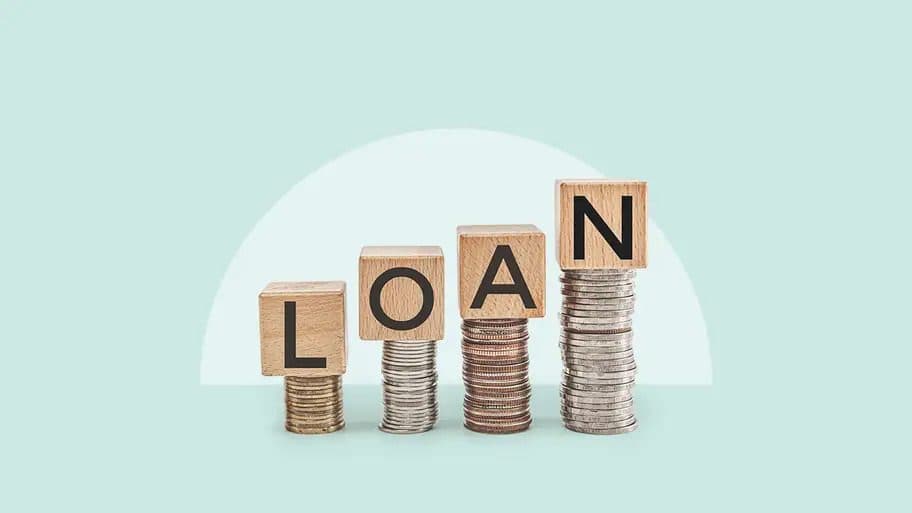 Wooden blocks spelling LOAN on rising stacks of coins
